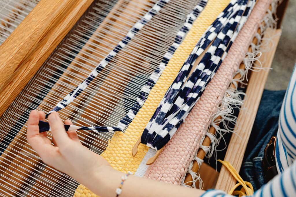 Detailed view of hands weaving a colorful textile on a loom, showcasing craftsmanship and artistry.